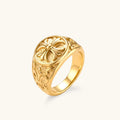 18K gold-plated stainless steel signet ring with ornate cross face and carved filigree scroll band, shown from three angles.