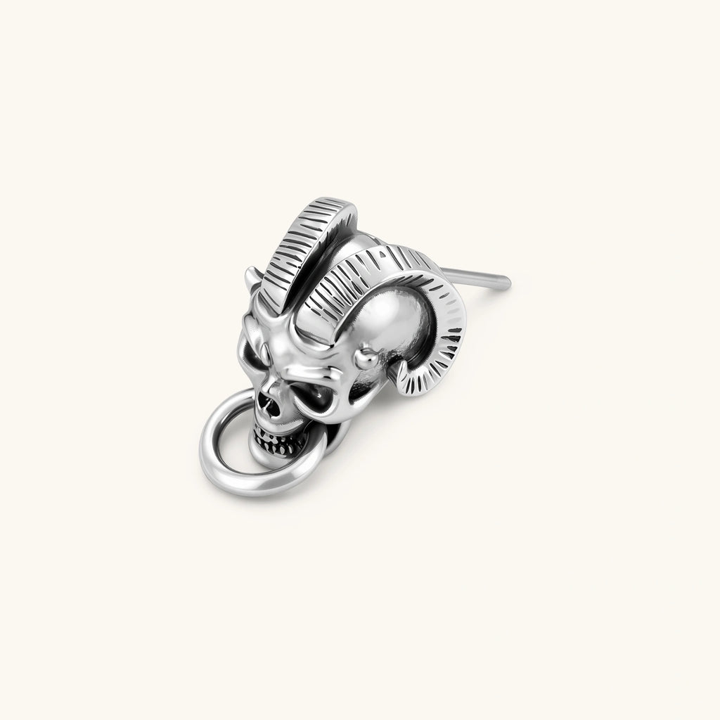 Silver 316L stainless steel stud earring shaped as a horned demon skull with ram horns and a dangling mouth ring.