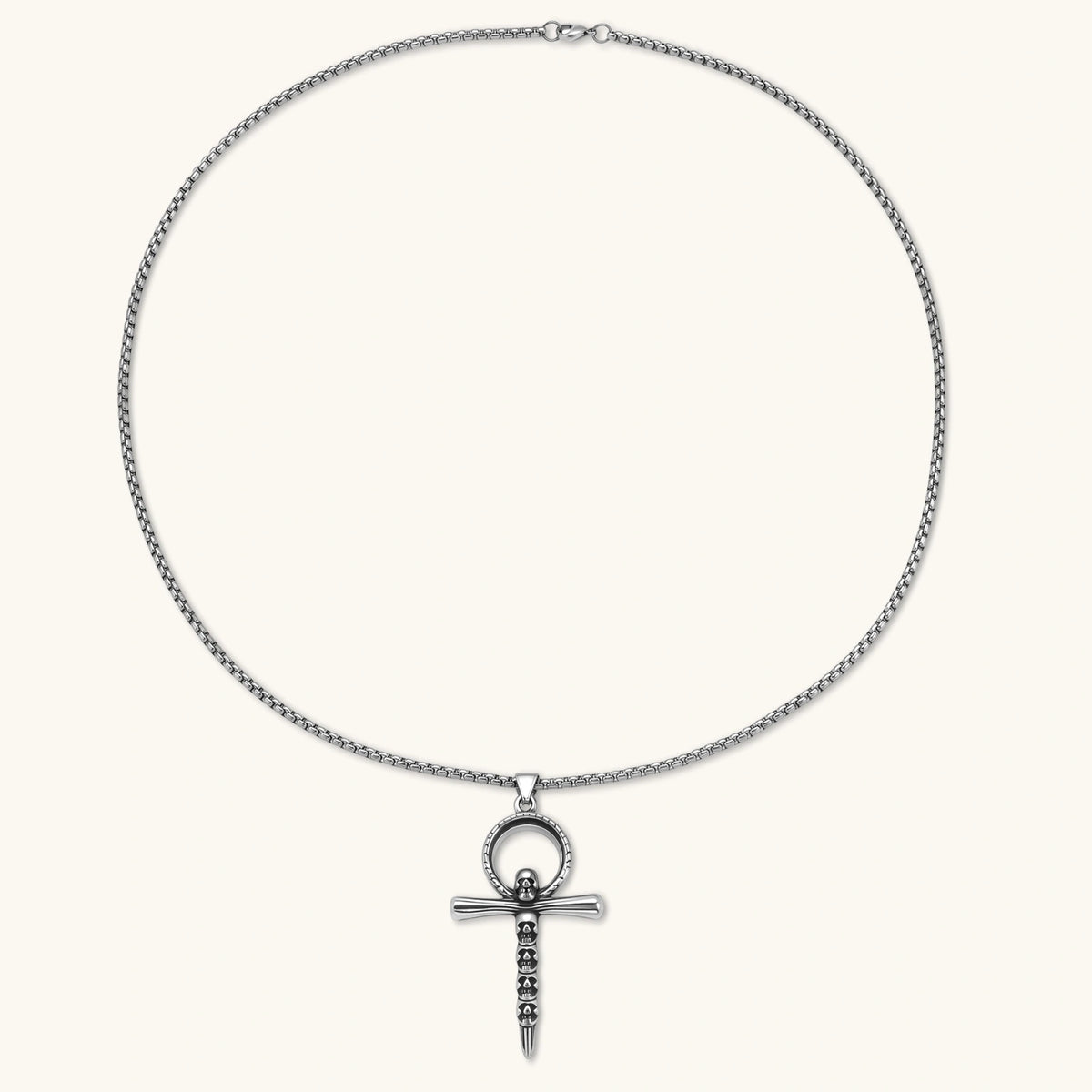 Silver stainless steel ankh pendant with skull motifs on vertical bar and textured ring top, on a box chain necklace.