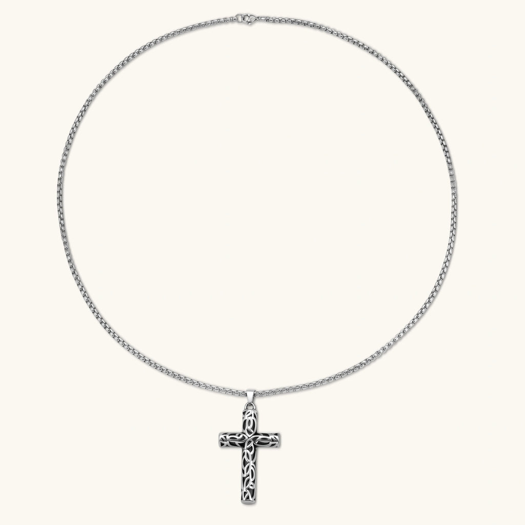 Silver stainless steel Celtic cross pendant with filigree vine pattern on a box chain, against a cream background.