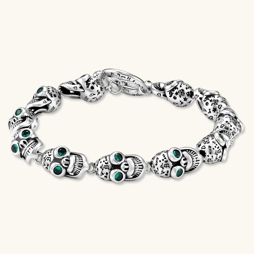 Silver stainless steel skull link bracelet with green crystal eye sockets and engraved detailing, toggle clasp closure.