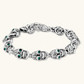 Silver stainless steel skull link bracelet with green crystal eye sockets and engraved detailing, toggle clasp closure.