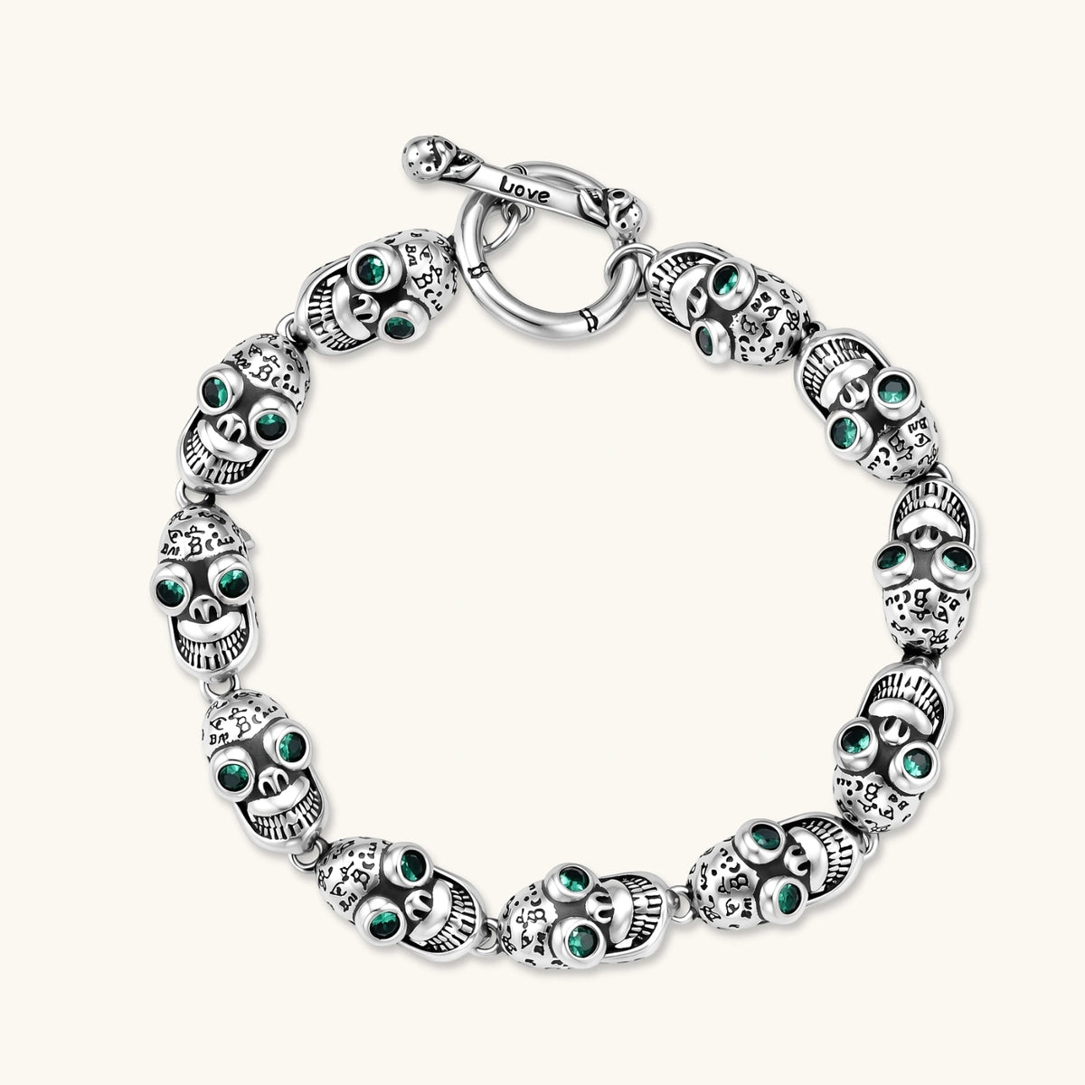 Silver stainless steel skull link bracelet with green crystal eye sockets and engraved detailing, toggle clasp closure.