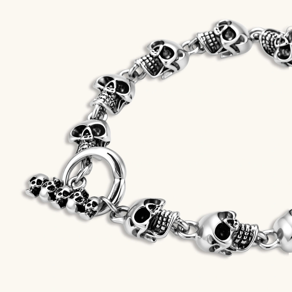 Silver stainless steel bracelet with linked 3D skull charms and a spring-ring clasp, oxidized black detailing, 225mm length.