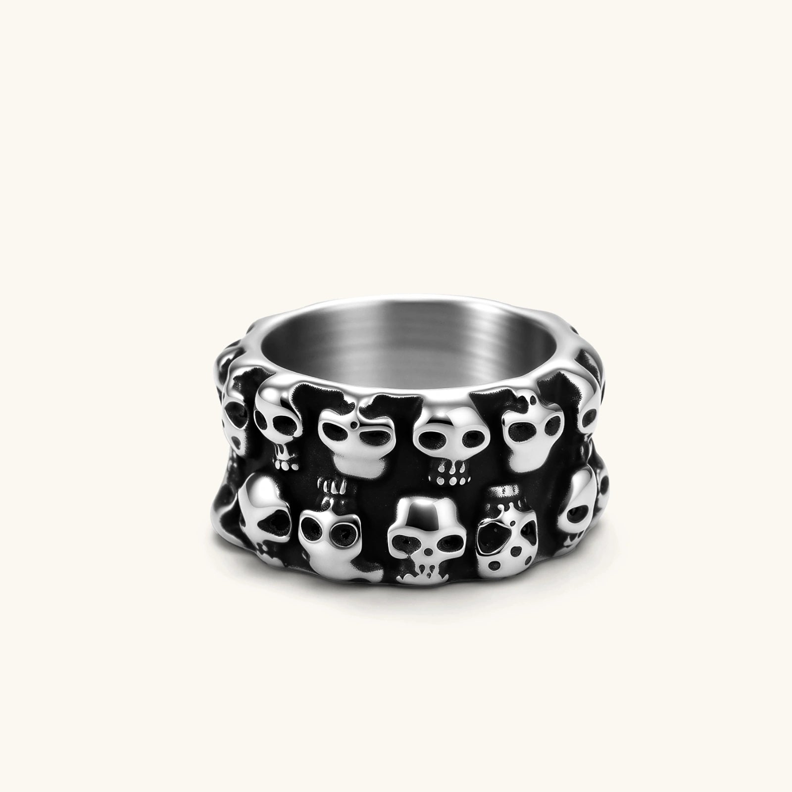 Wide stainless steel ring with raised 3D skull cluster design, black oxidized recesses, brushed silver interior, side angle view.